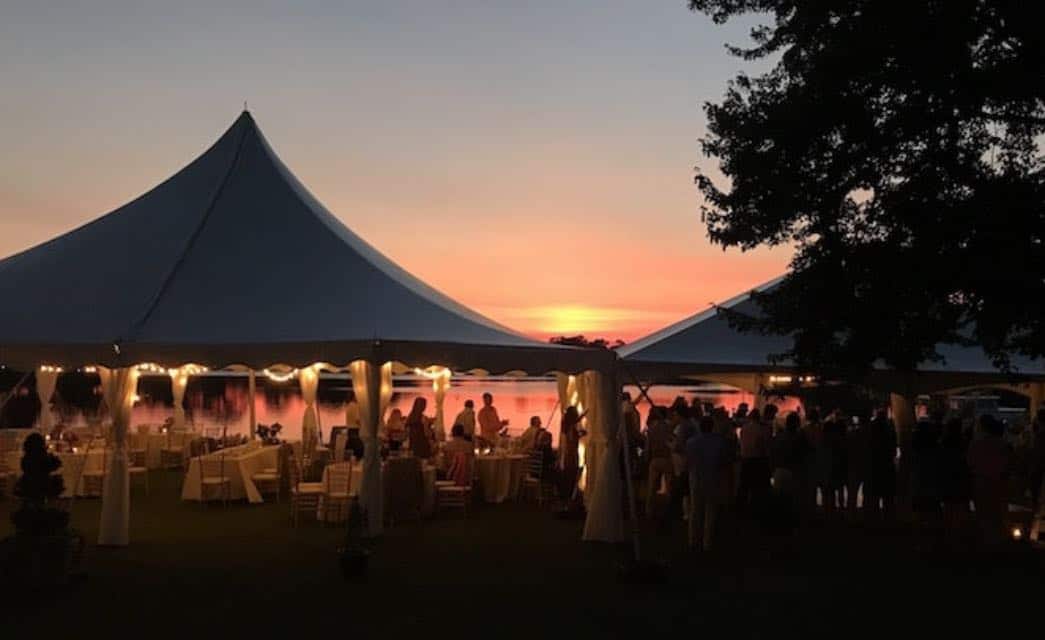 Two large white tents set up near the water for an event at dusk