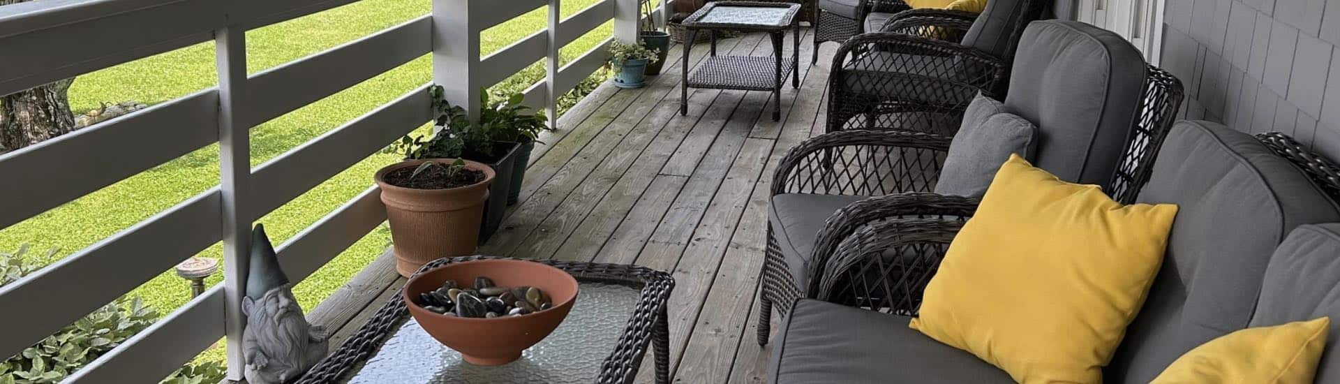 Gray wicker patio furniture with gray cushions and yellow pillows on a wooden balcony with gray railing