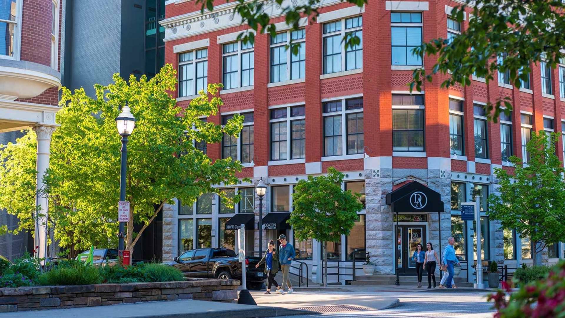 Close up view of a downtown building with green trees and people walking on the sidewalk