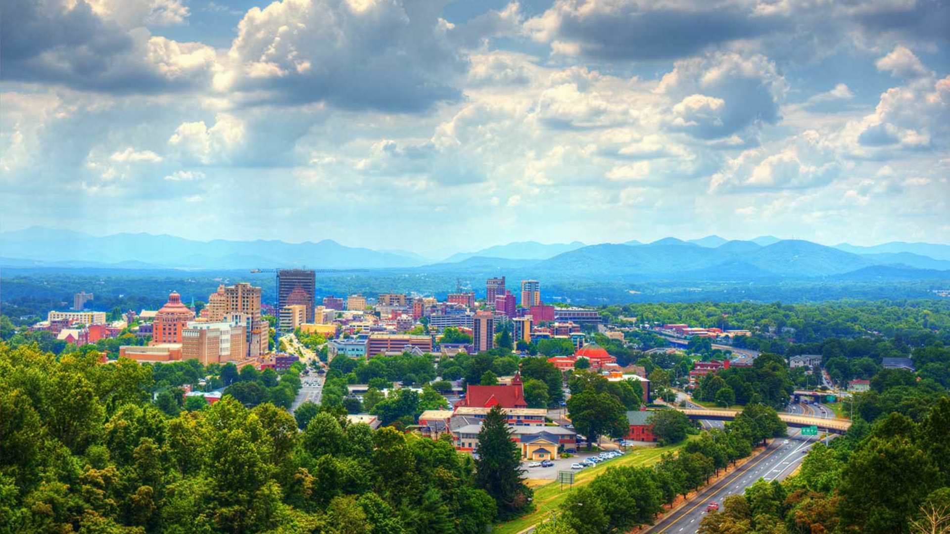 Aerial view of downtown buildings surrounded by green trees and mountains in the background