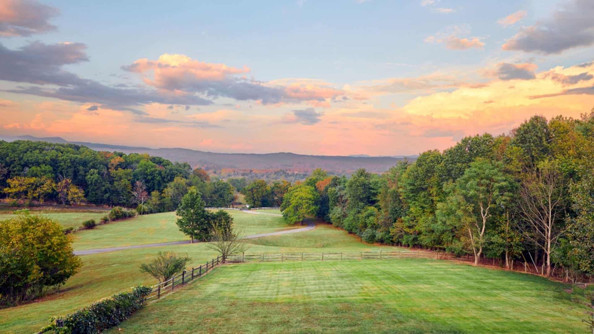 Large green lawns surrounded by large trees with hills in the background at dusk