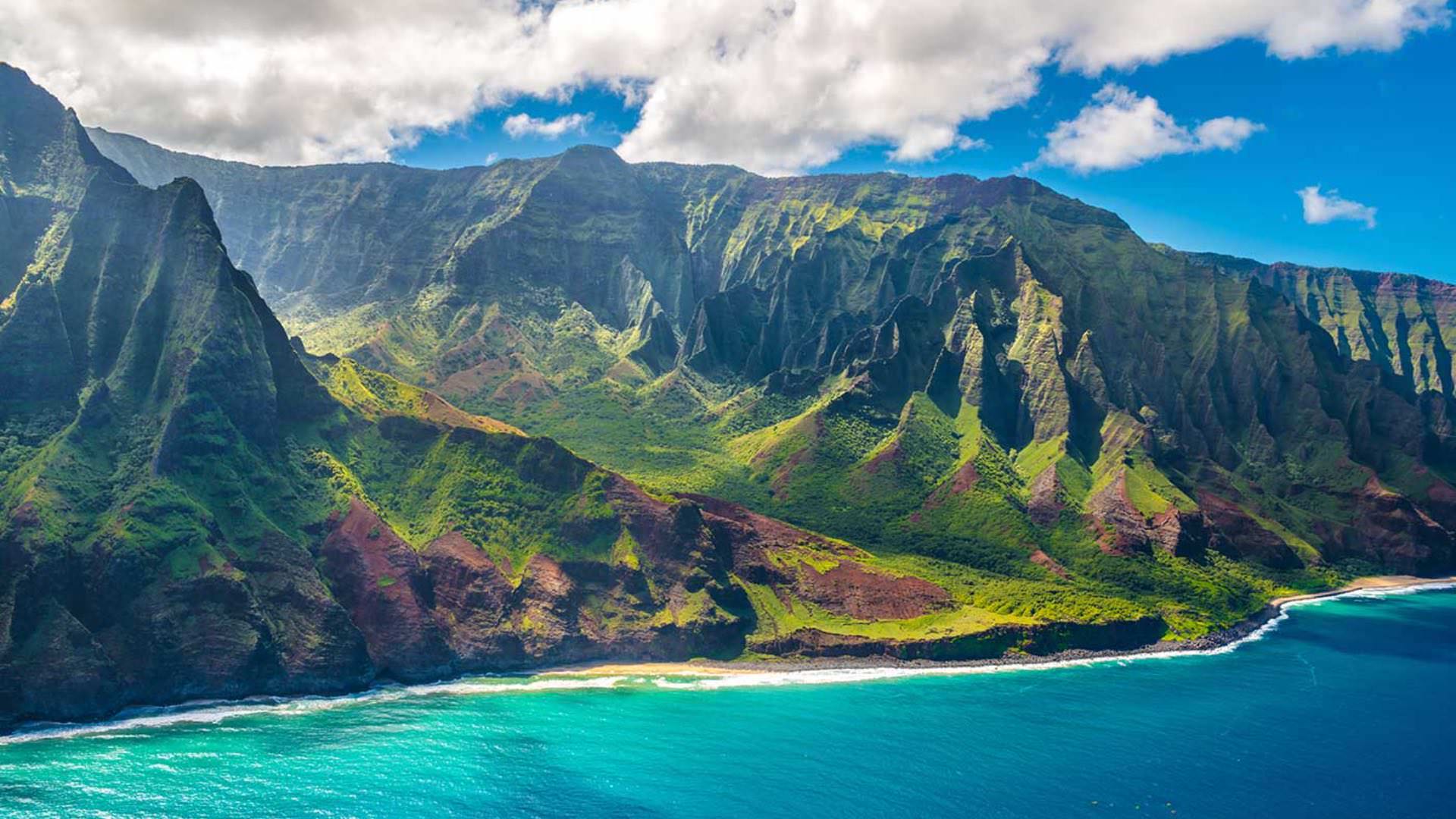 Aerial view of mountains covered in moss next to bright blue ocean water