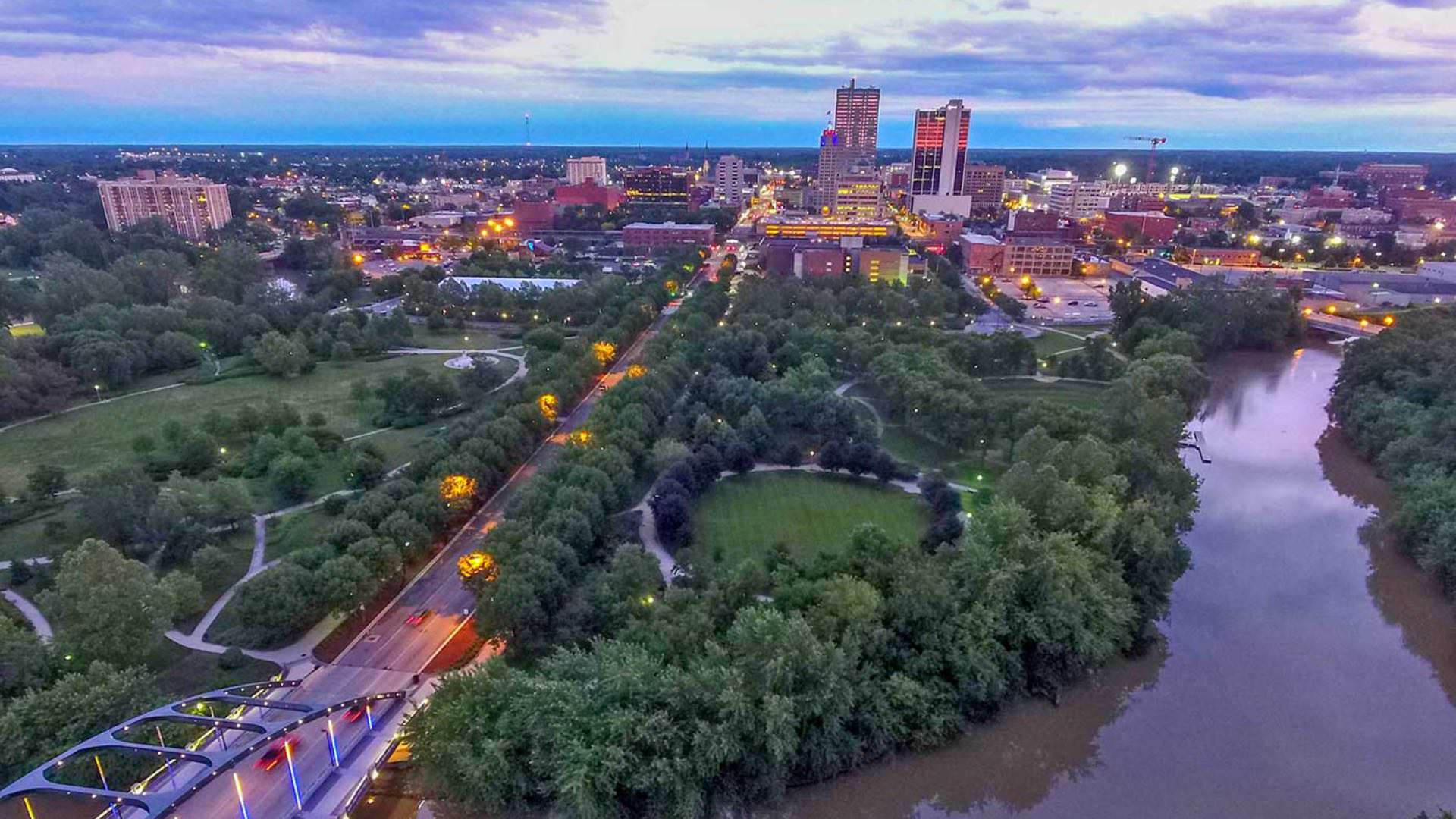 Aerial view of a downtown city with multiple parks, green trees, and small river winding through