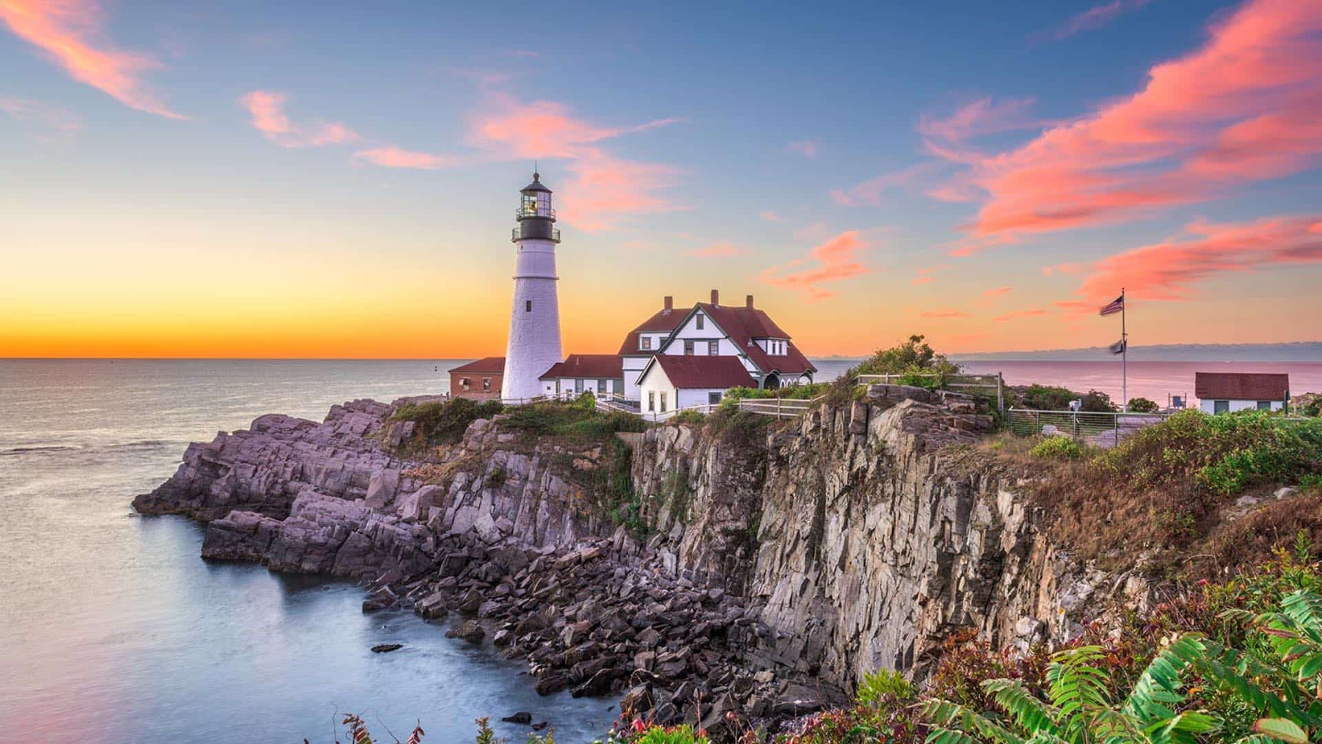 White lighthouse and house on a rocky cliff next to the water