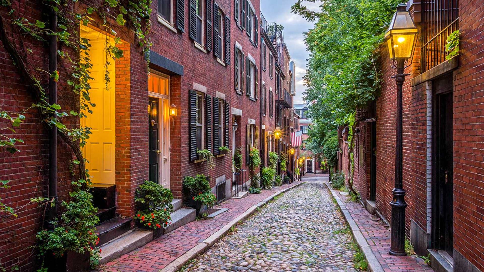 Narrow cobblestone path between two red brick buildings leading down to a street