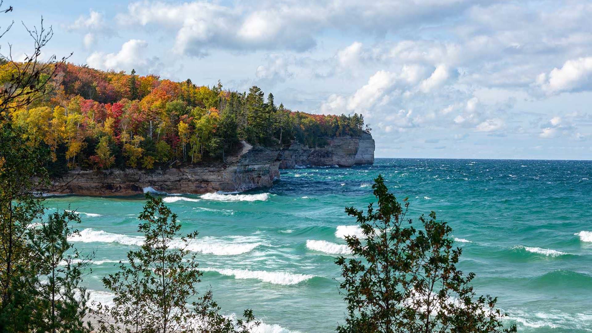 Rocky cliffs covered in red, orange, yellow and green trees near the water