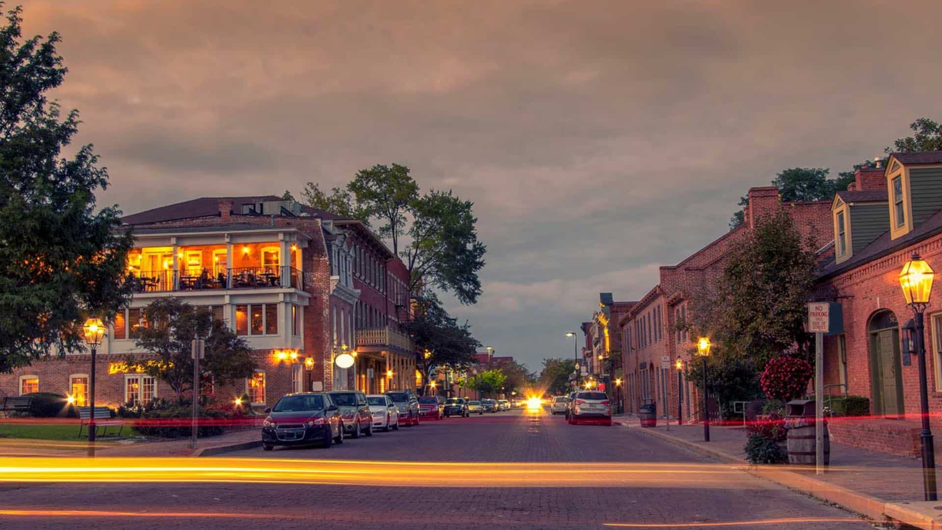 Small downtown brick street with multiple red-bricked buildings all lighted up at dusk