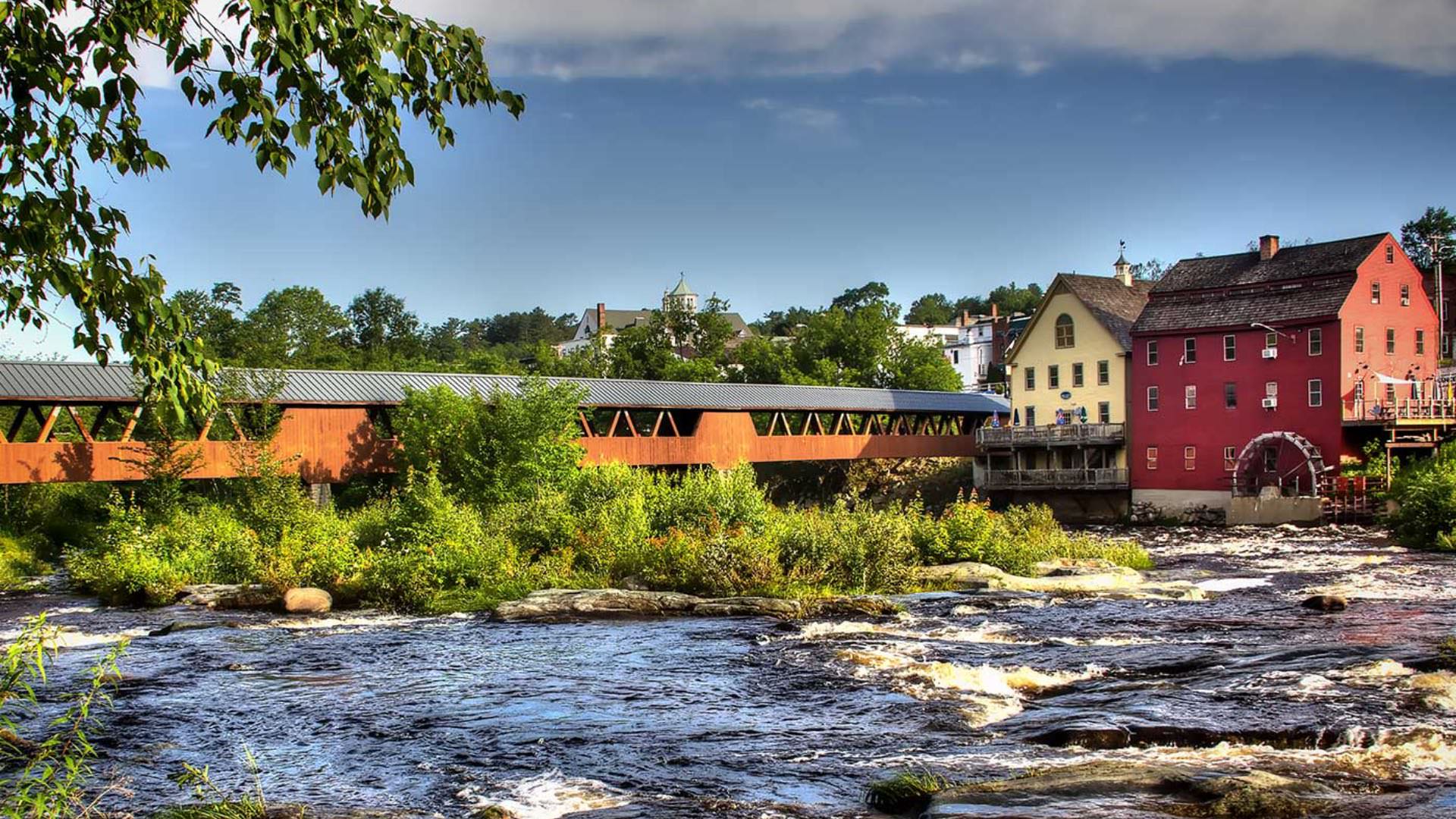 Long wooden bridge over fast-moving river leading into a small town