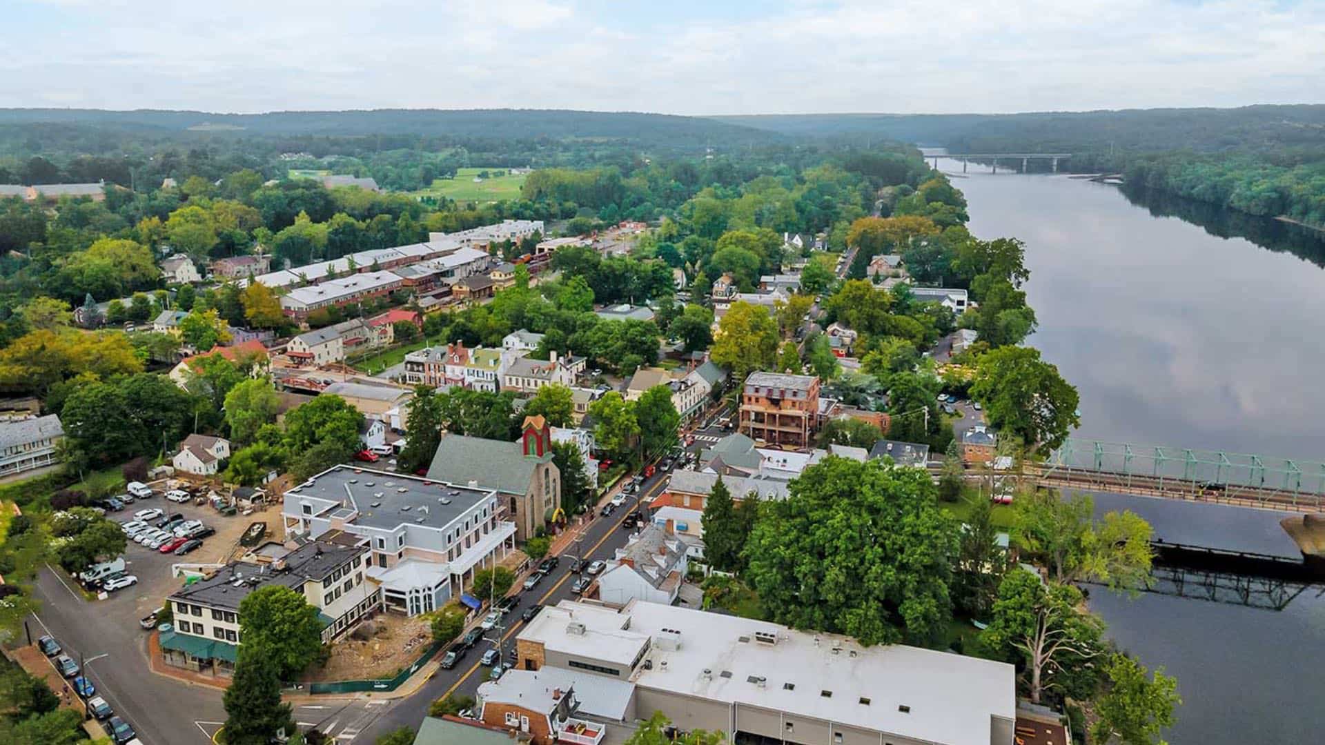 Aerial view of a small town's downtown area with large green trees and next to a small river