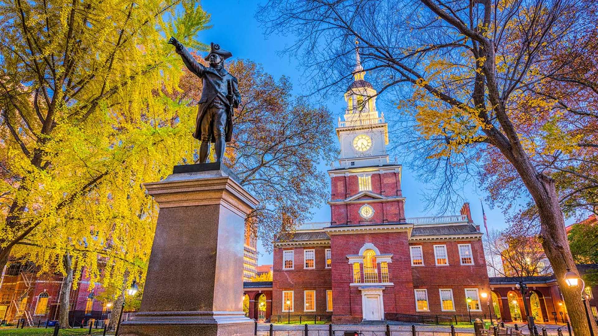 Bronze statue with large red-bricked building in the background lighted up at dusk