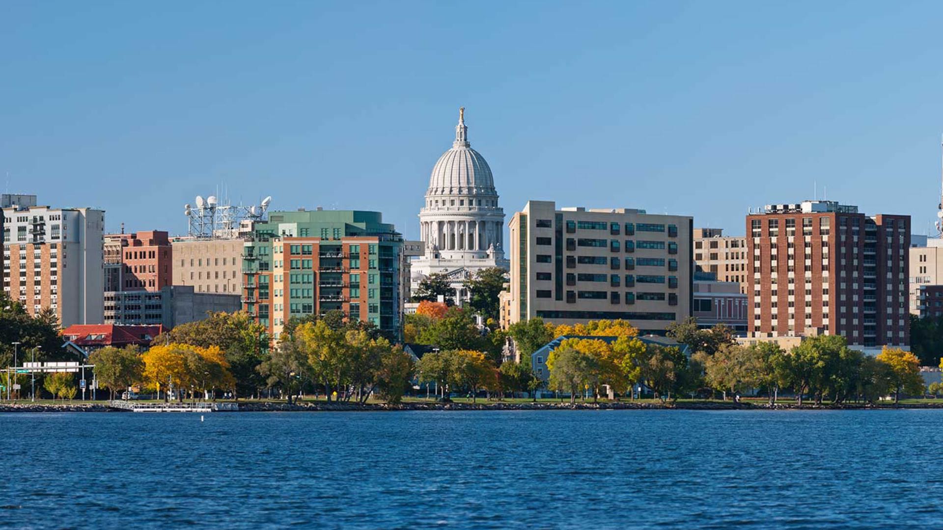 Downtown view of a city's capitol building surrounded by other buildings and a body of water