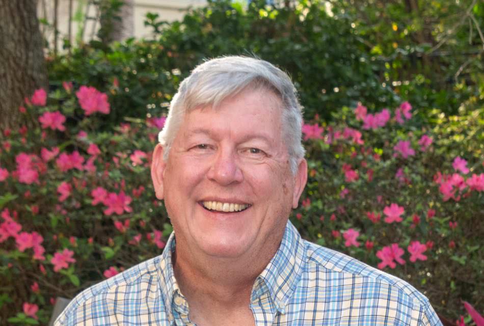 Man wearing a blue and yellow plaid shirt standing in front of large bush with pink flowers